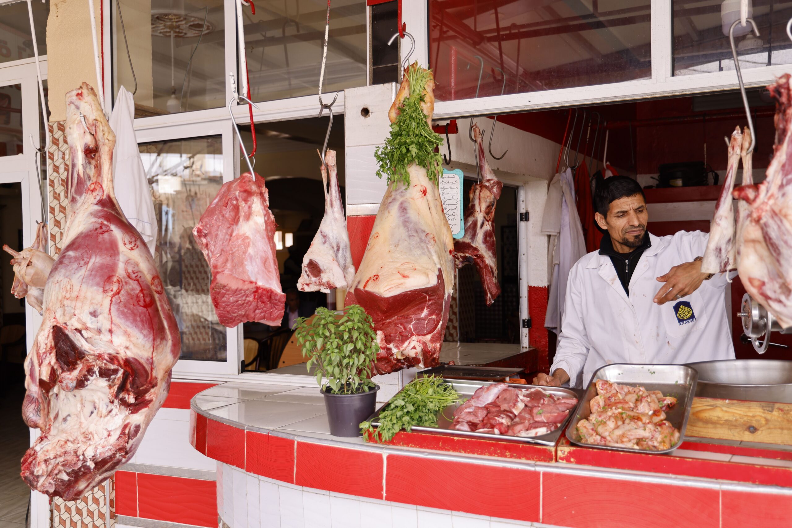 A butcher working at an outdoor market stall with various cuts of beef hanging, showcasing fresh meat preparation.